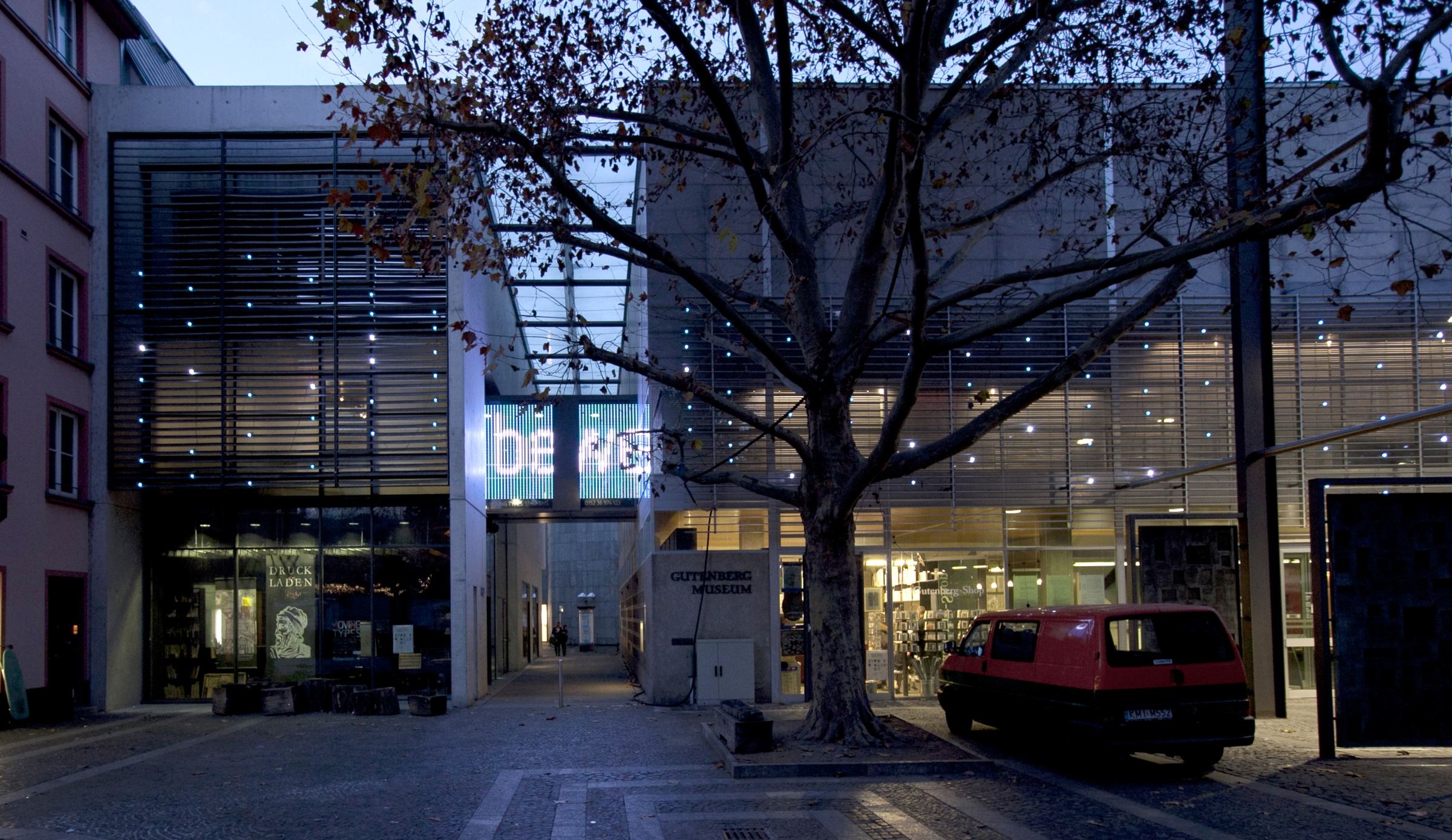 The Gutenberg-Museum at dusk: single points of light scattered across the whole façade, and letters glowing on the glass bridge in the middle