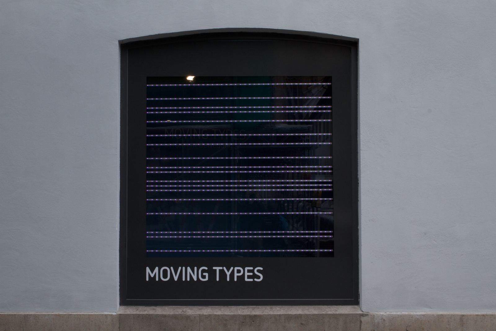 An arched window of the Galerie im Prediger filled with rows of LED bars, the words Moving Types below