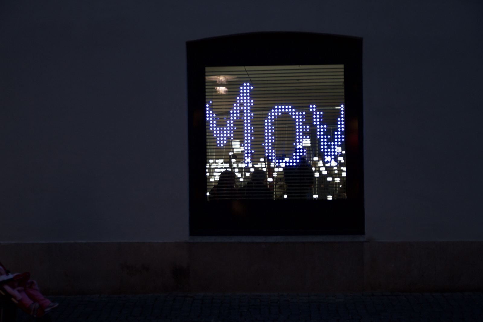 The same window at night, glowing letters M, o and v passing through it