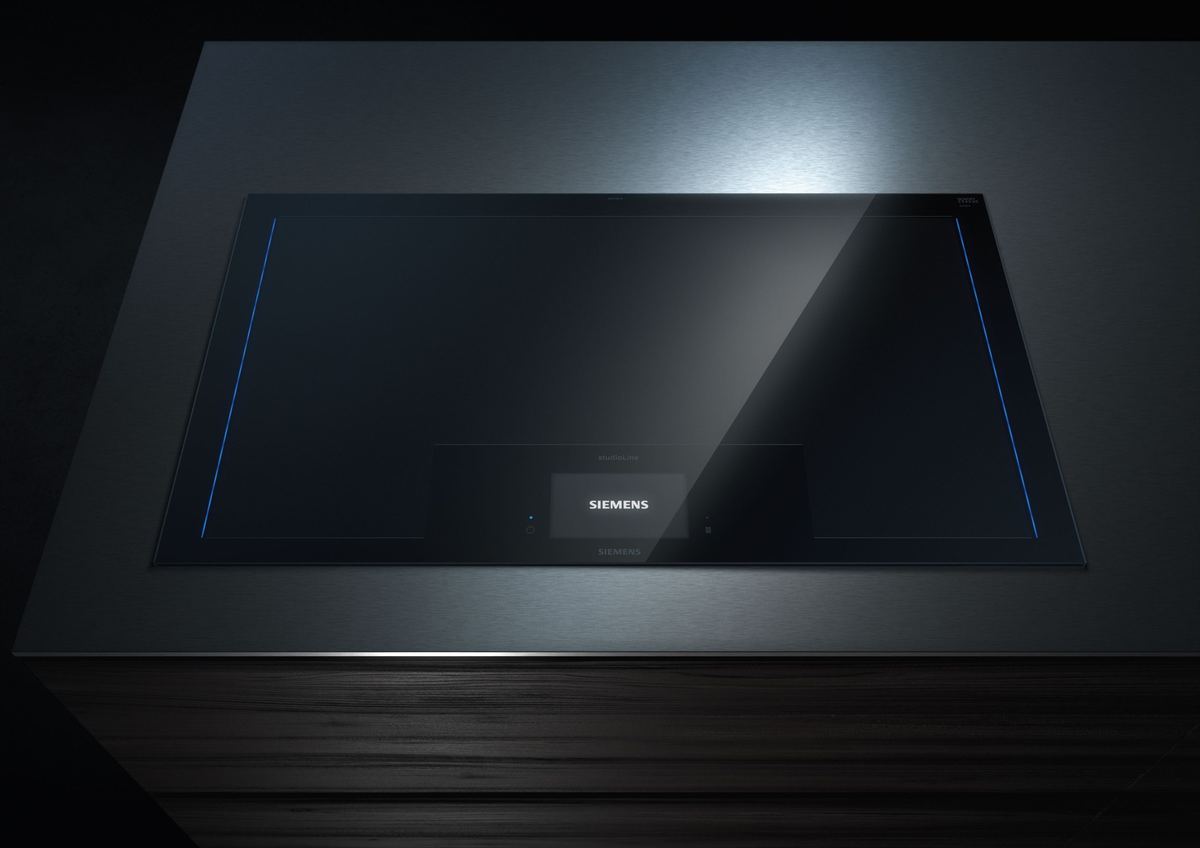 The empty cooktop in a dark kitchen island, with thin blue light lines in the glass and the display at the front