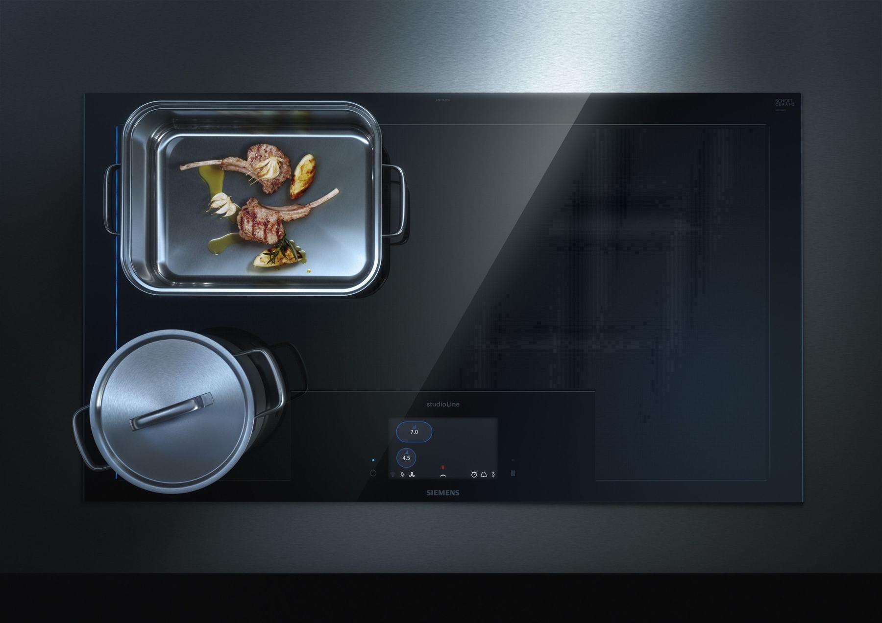A roasting tray and a pot on a dark free induction cooktop, seen from above. The touch display sits at the front edge.